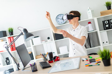 A young man in virtual reality glasses stands near the table and pulls his arm up. A young man thumbs a virtual page.