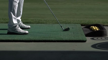 Young golfer practices his golf swing on driving range, view from side