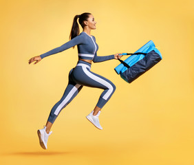 Fototapeta na wymiar Go to training. Sporty woman with bag running in silhouette on yellow background. Dynamic movement. Side view. Sports and healthy lifestyle