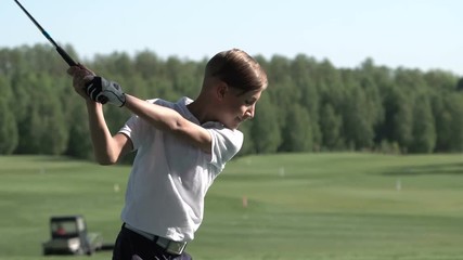 Junior golfer playing golf on summer with hitting shot on green grass