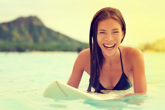 Happy Asian girl taking a surf class having fun surfing on surboard in Waikiki beach, Honolulu, OAHU, HAWAII. Joyful woman laughing enjoying summer travel holidays.
