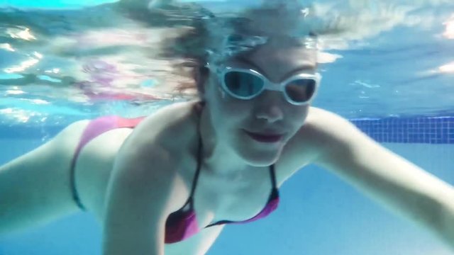 Young pregnant woman swimming underwater in goggles removes itself on an action camera POV