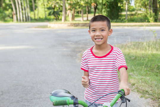 Cute Asian Boy Ride A Bicycle In A Park.