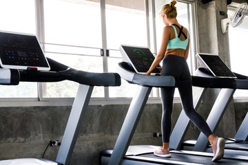 Fototapeta na wymiar Young woman running on the treadmill at the gym