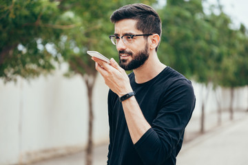 Leisure, technology, communication and people concept - young man using voice command recorder or...