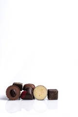 Selection of six chocolates in the bottom, on a glossy white surface, with a white background. 
