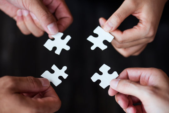 hand of people holding jigsaw puzzle pieces and try to solving puzzle together , team work concept