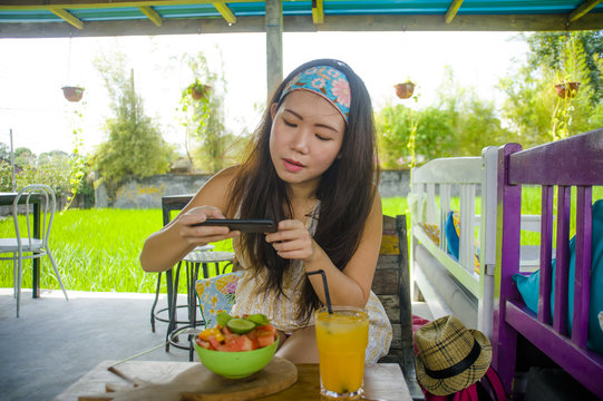 young happy and pretty digital nomad Asian Chinese woman taking picture of fruit salad with mobile phone networking on internet social media