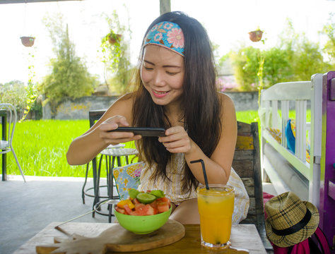 young happy and pretty digital nomad Asian Korean girl taking picture of fruit salad with mobile phone networking on internet social media