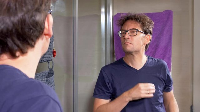 Man with glasses checking himself in mirror after shaving