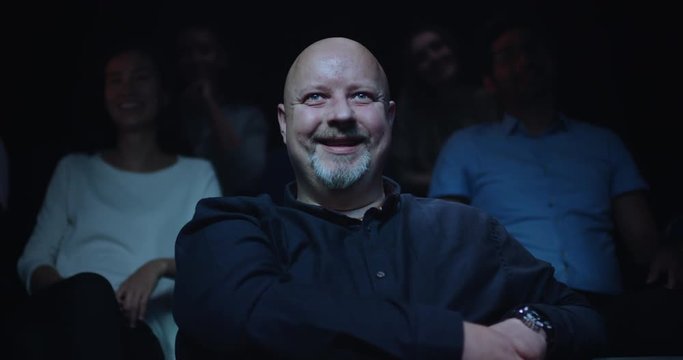 A smiling/laughing man watching a movie in the movie theatre.