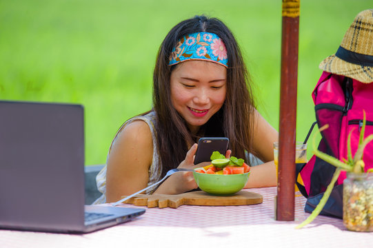 young happy and pretty digital nomad Asian Chinese girl taking picture of fruit salad with mobile phone networking on internet social media