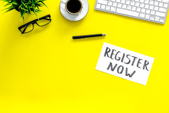 Membership concept. Template for registration. Register now hand lettering iconon word desk with glasses, coffee, plant, computer keyboard on yellow background top view copy space
