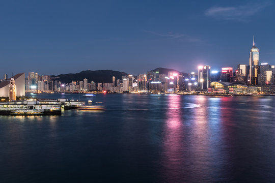 The Star Ferry pier in Tsim Sha Tsui in Kowloon with the skyline of Hong Kong island business district around Wanchai in the background across the Victoria harbor.