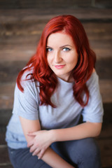 Young woman with red long hair indoor portrait on wooden background