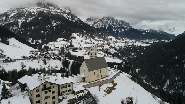 aerial drone flying above small church in italian alps at cludy winter day