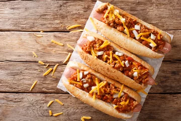 Gardinen Chilischoten Traditional American chili hot dogs with cheddar cheese, onion and spicy sauce closeup. Horizontal top view  © FomaA