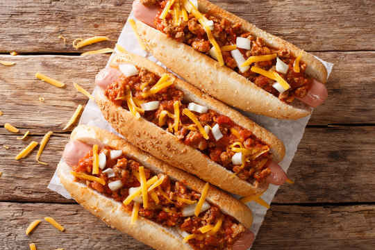 Authentic chili hot dog with cheddar cheese, onion and spicy sauce close-up on paper. Horizontal top view