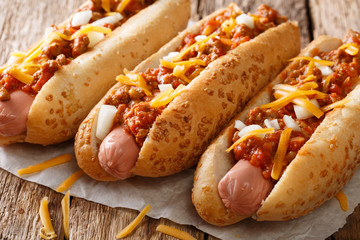 Authentic chili hot dog with cheddar cheese, onion and spicy sauce close-up on paper. horizontal