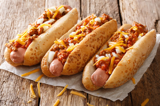 Three tasty chili hot dogs with cheddar cheese, onion and spicy sauce close-up on paper. horizontal