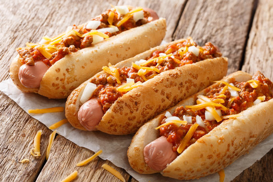 Traditional American chili hot dogs with cheddar cheese, onion and spicy sauce closeup. horizontal
