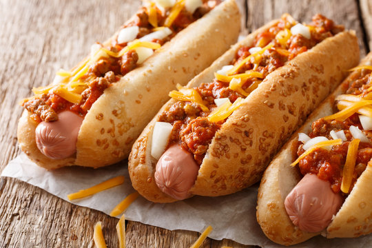 American fast food: chili hot dogs with cheddar cheese, spicy beef mince, onion and sauce close-up on the table. Horizontal