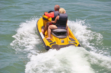 An older senior couple riding tandem on a bright yellow jet ski on the Florida Intra-coastal Waterway near Miami Beach.