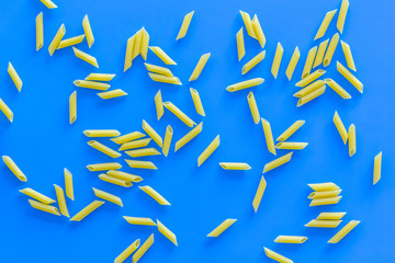 Pasta background. Raw penne on blue background top view