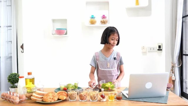 Little girl learning online cooking with using laptop computer in the kitchen at home  