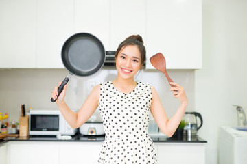 Happy housewife hold up with pan wooden turner in kitchen