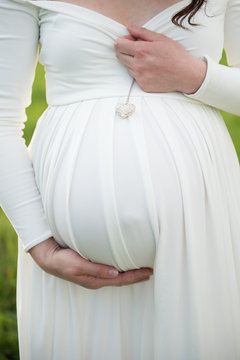 woman wearing white dress holding pregant belly 