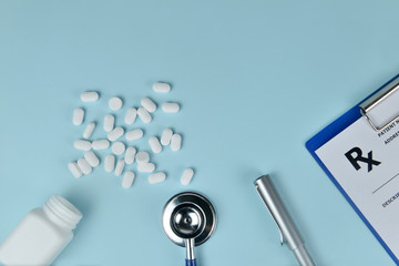 Top view of doctor desk with medical equipment. Stethoscope, thermometer, prescription clipboard and  white bottle of pills on blue background with text space. Health care and medical concept.
