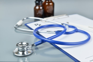 Close up stethoscope with prescription and medicine bottle on opaque glass background.