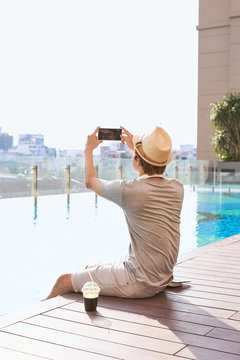 Asian man using a smartphone to take a photo of swimming pool background