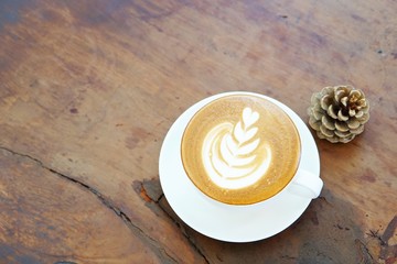 A white cup of coffee with latte art, pine cone on wooden table, top view, copy space
