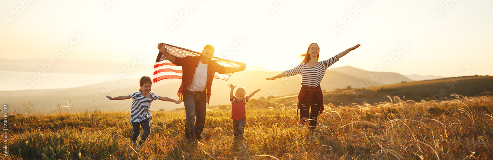 Wall mural happy family with flag of america USA at sunset outdoors.