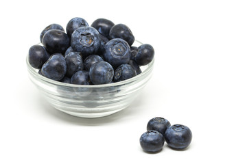 Bilberry in the transparent bowl and three berries separately on the white background