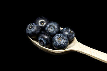 A wooden spoon full of ripe blueberries on the black background. Fresh ripe juicy bilberries.