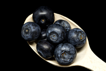 Macro of a wooden spoon full of ripe blueberries on the black background. Fresh ripe juicy bilberries.
