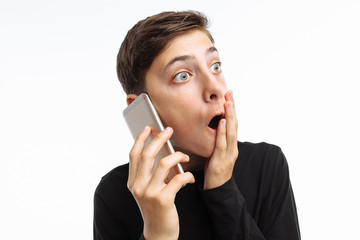 Portrait of a teenager, a guy holding a phone, looking at the phone and shows the emotion of surprise on his face, in a black t-shirt, on a white background, advertising, text insert