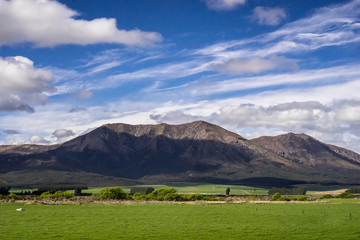 New Zealand scenery mountains and green grass field with cloudy blue sky over the mountain