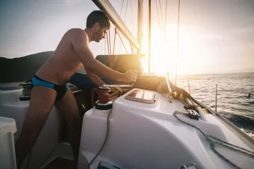 Crédence de cuisine en verre imprimé Naviguer Sailor pulling rope on sailboat on the sunset sea  