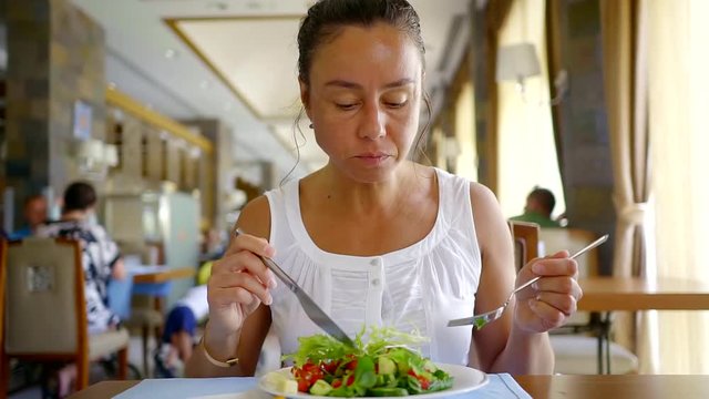 Close up portrait of adult brunnete woman eating light salad in a cafe.