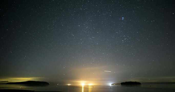 Stars moving across sky above Washington's Puget Sound with city lights in distance.