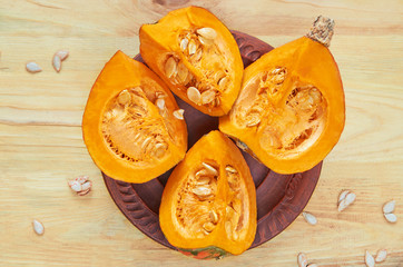 Pumpkin slices with seeds on the brown plate on the wooden background. Ingredients for tasty autumn dish. Top view