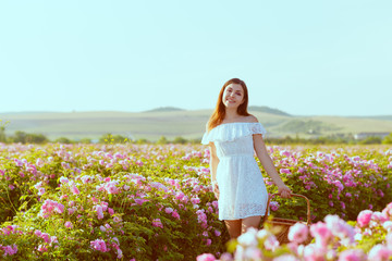 Obraz na płótnie Canvas Beautiful young woman posing near roses in a garden.