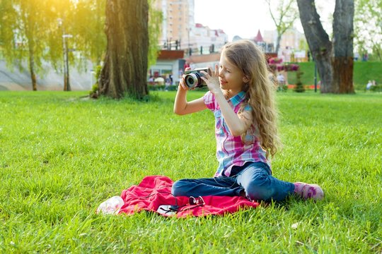 Little girl child of 8 years looking at camera sitting on green lawn in city park.