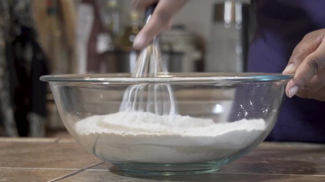 Closeup, black woman whisks flour with dry ingredients in a glass bowl