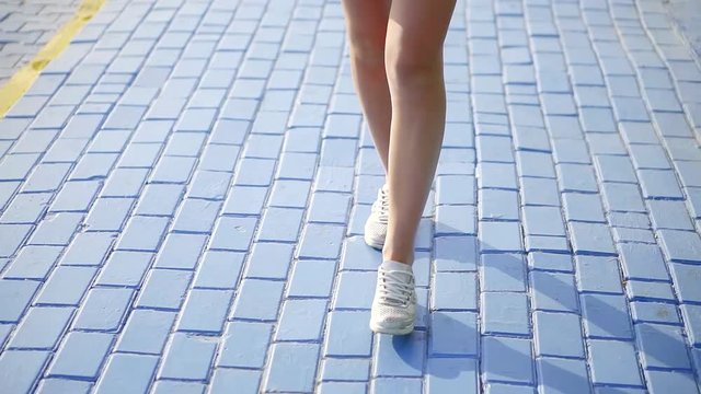 Close up shot of woman walking on the sidewalk wearing sneakers and skirt in summertime.