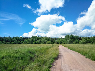 Fototapeta na wymiar Country road through a green field on a sunny day with clouds.